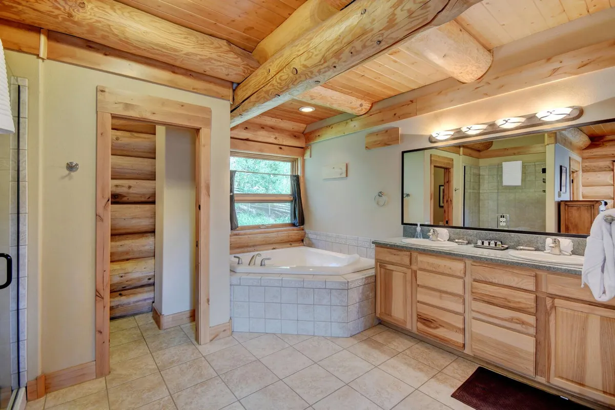 A luxurious bathroom where sunlight streams through the window onto a freestanding bathtub with natural wood accents. A large mirror reflects the tranquil space, emphasizing relaxation and comfort.