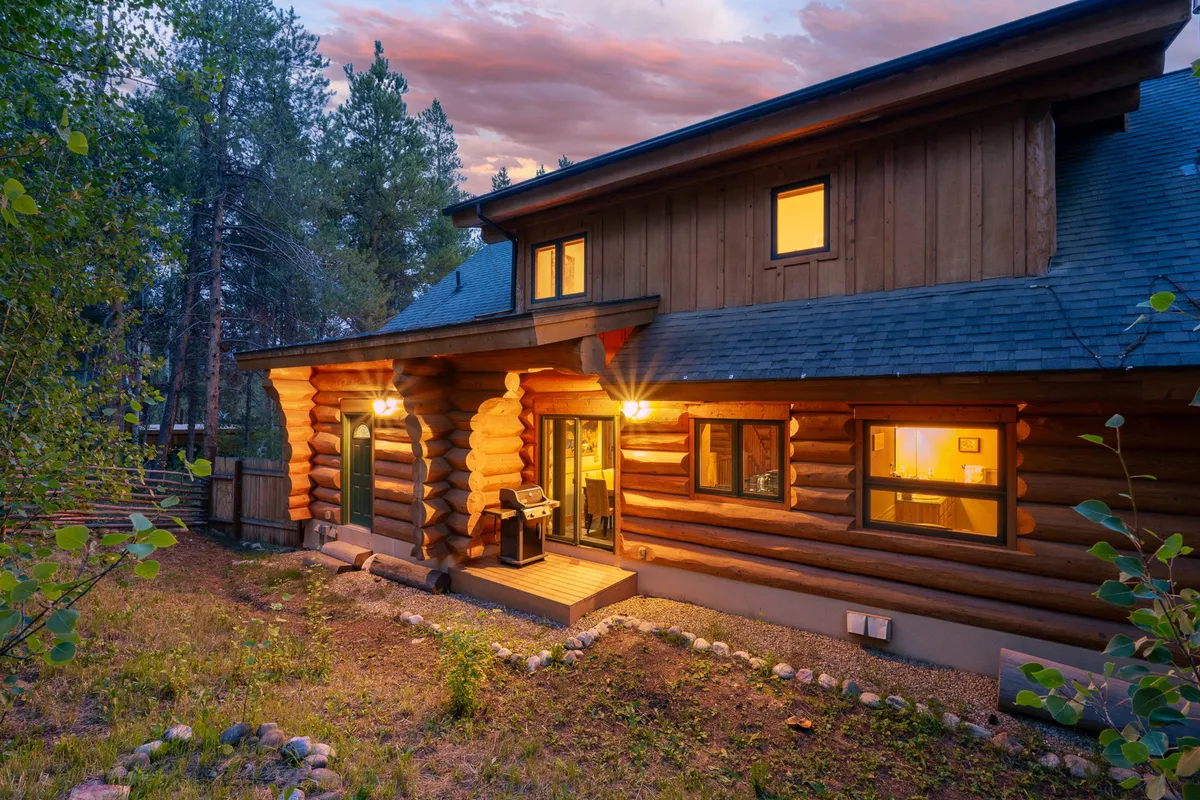 This image shows the log cabin's warmly lit exterior and front porch, set against the peaceful backdrop of the mountain environment. The inviting atmosphere hints at evenings spent outdoors, enjoying sunsets or gatherings, and emphasizes the cabin's welcoming and serene qualities.