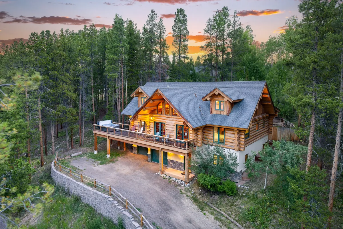 This image displays a classic log cabin structure nestled among trees, featuring large windows and an inviting deck area. The tranquil setting is emphasized by the surrounding natural landscape, suggesting the privacy and immersive mountain experience described in the section. The deck is positioned to enjoy scenic views and wildlife, perfectly matching the narrative of outdoor serenity.