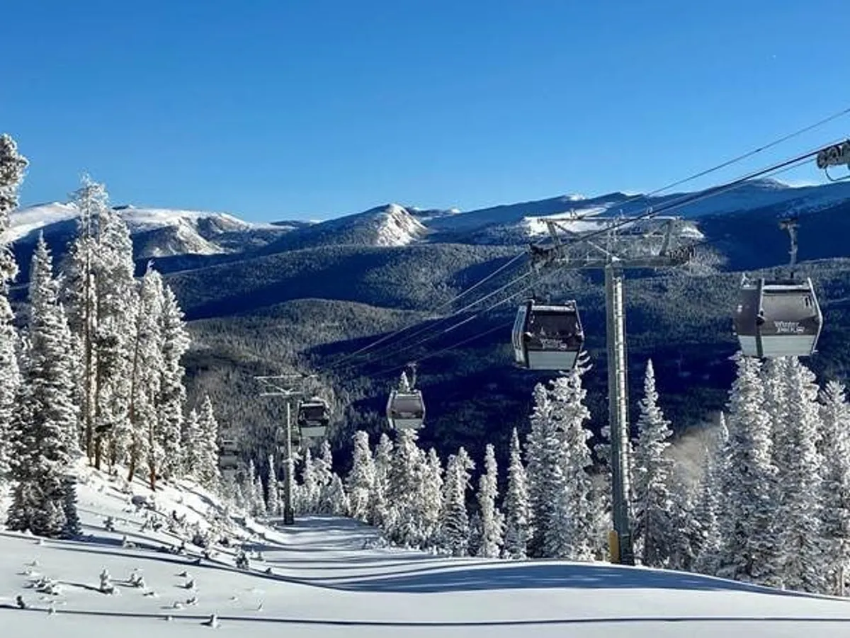 A sweeping winter scene captures ski lift gondolas gliding above pristine, snow-covered slopes surrounded by snow-blanketed trees and distant mountain peaks. The atmosphere feels both adventurous and serene, with clear blue skies and skiers dotting the landscape.